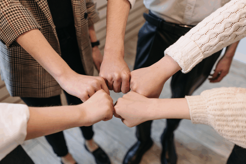 A photo of a group of people standing in a circle with their fists touching in solidarity - like they are a team. 